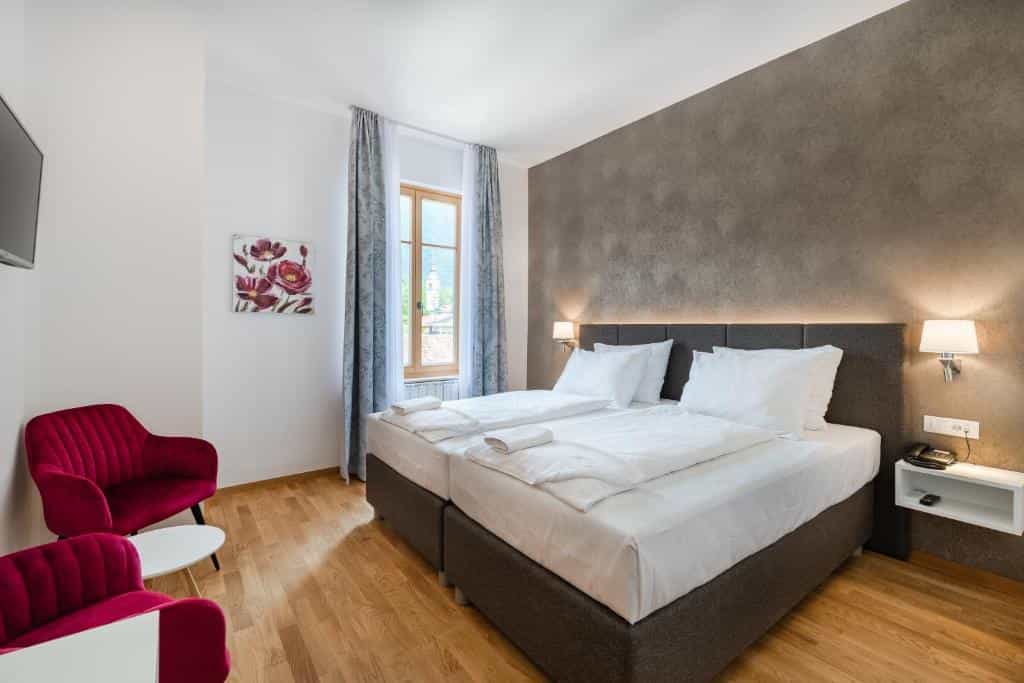 Hotel room with twin beds, red velvet chairs, and view of a distant steeple through the window.