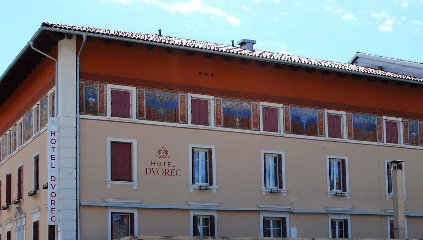 Hotel Dvorec building facade with painted frieze and vertical sign against a blue sky.