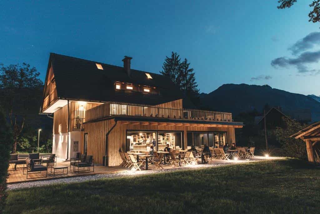 Wooden hotel exterior with illuminated terrace dining at dusk near mountains, Hotel Majerca.
