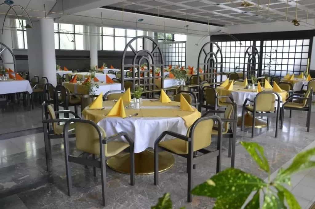 Hotel dining room set with yellow tablecloths, white linens, and yellow napkins.