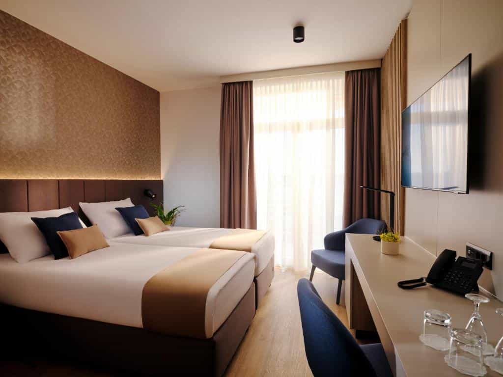 Twin beds in modern hotel room with textured brown accent wall and sheer curtains.