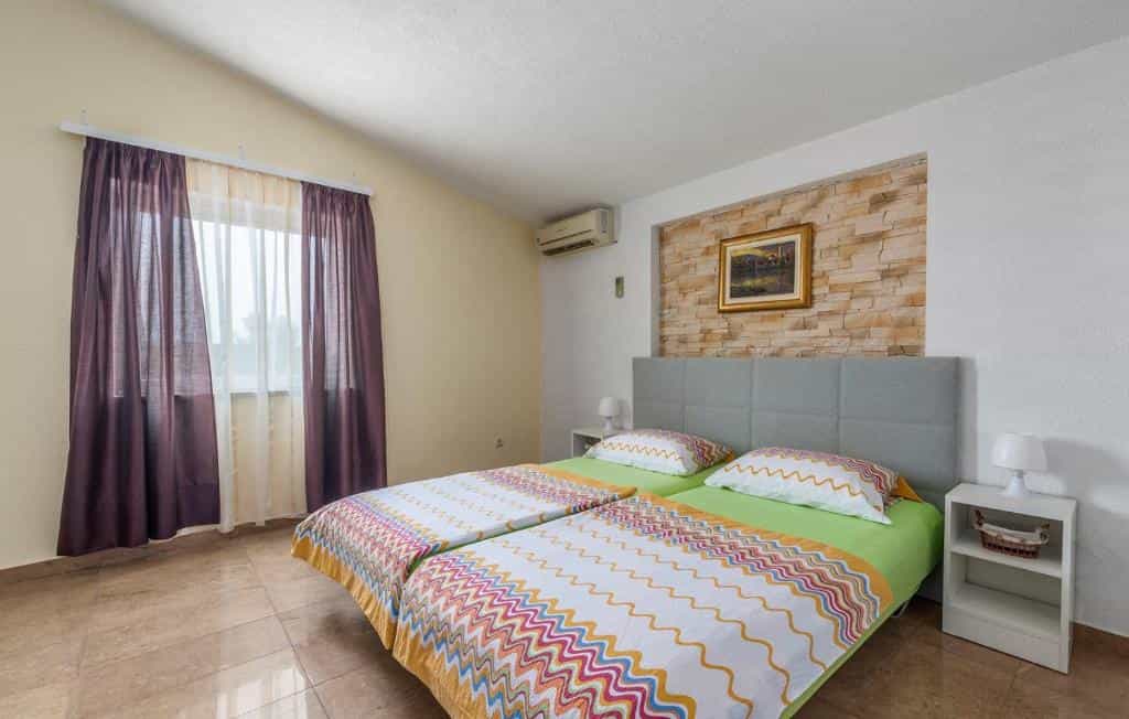 Twin beds with colorful zigzag bedding in a room with stone accent wall, Visnjan