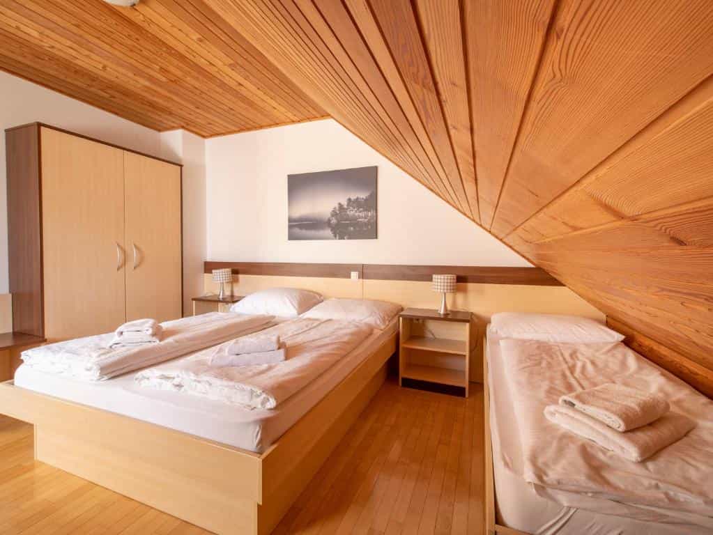 Hotel room with wooden sloped ceiling, two beds with white linens, and light wood furniture