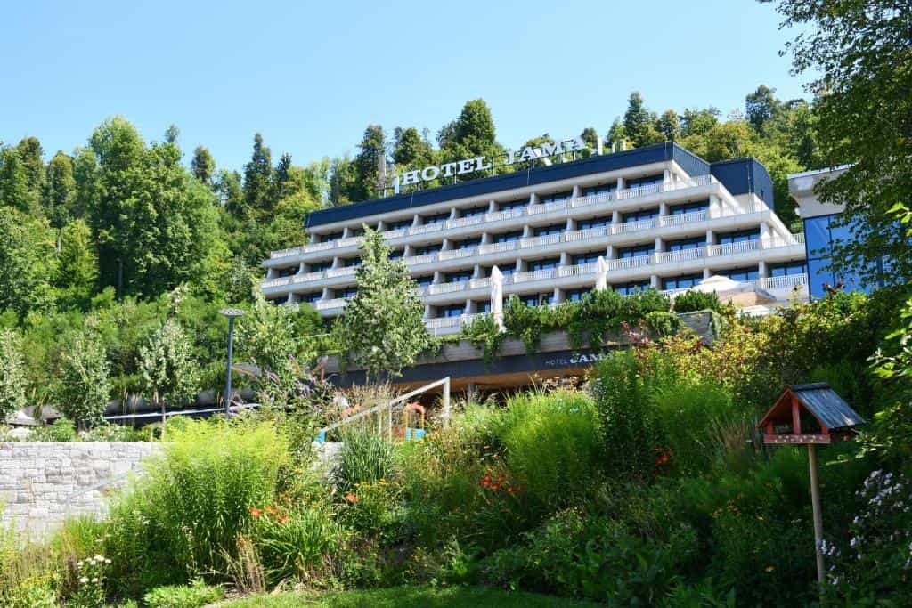 Hotel Jama building seen through lush green foliage and trees under a clear blue sky.
