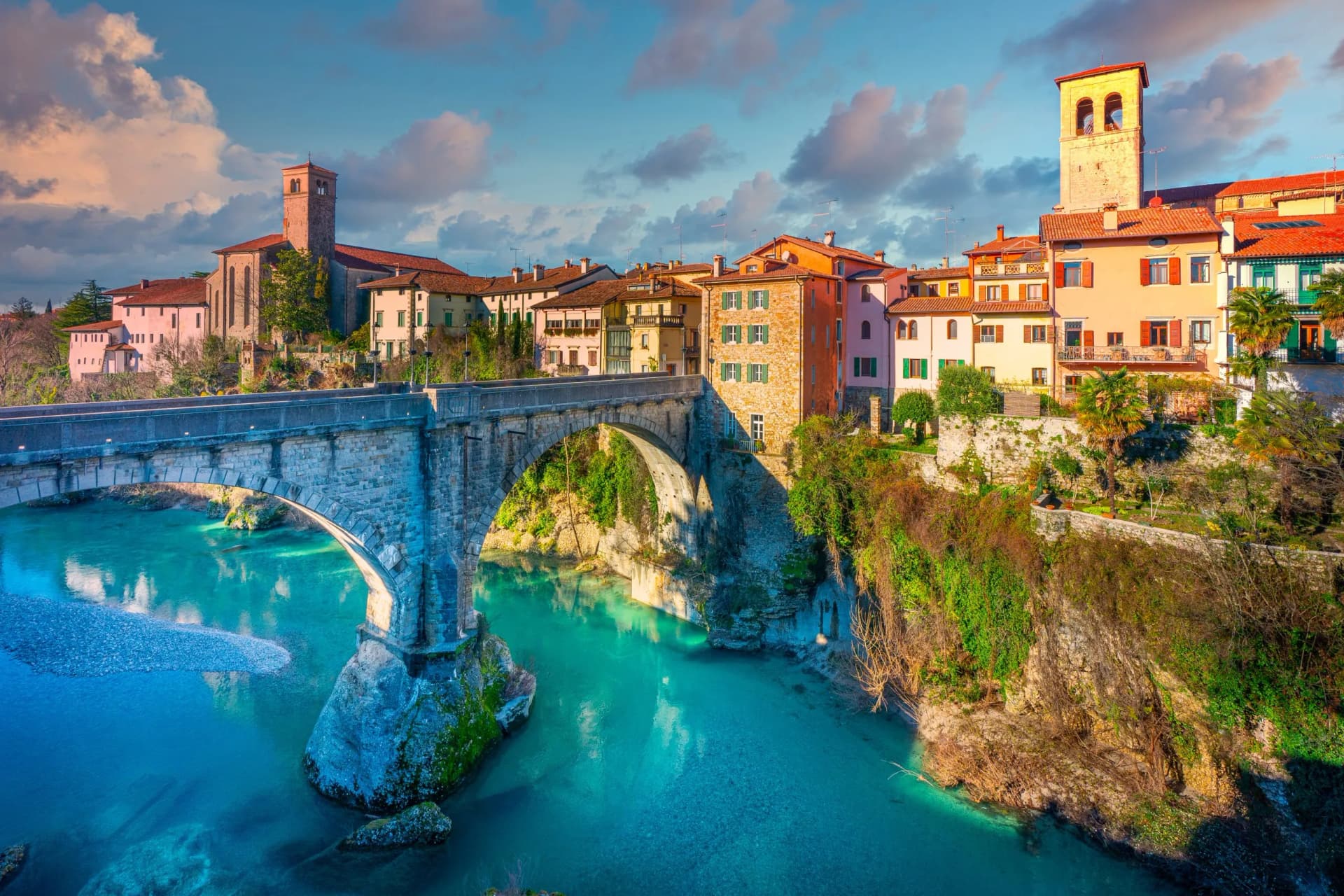 Stone arch bridge over turquoise river next to colorful buildings in Cividale del Friuli.