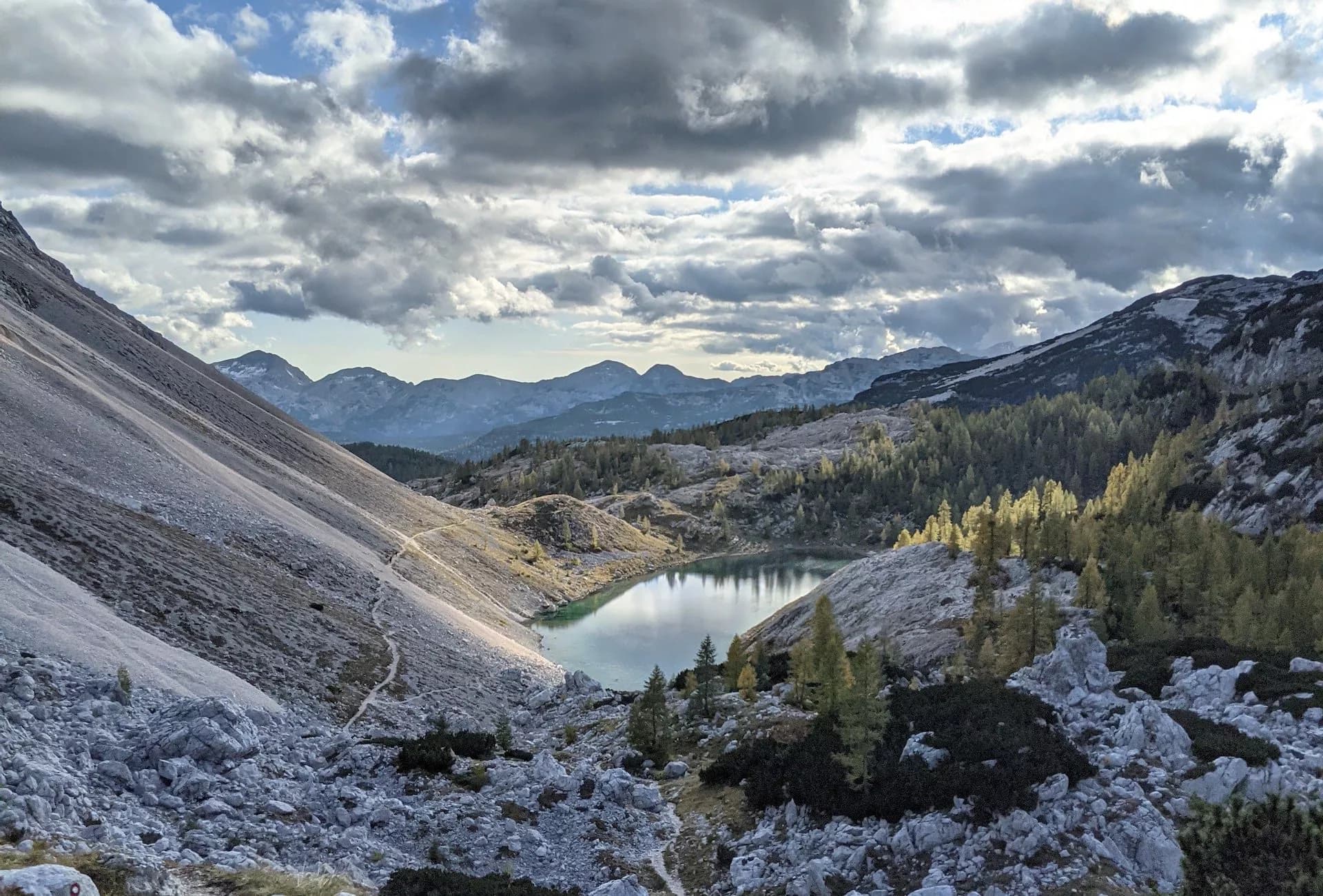 Mountain lake surrounded by rocky slopes and autumn trees under dramatic clouds in the Seven Lakes Valley.