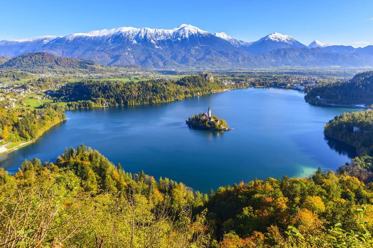 Panoramic view of Lake Bled island church with snow-capped mountains in autumn