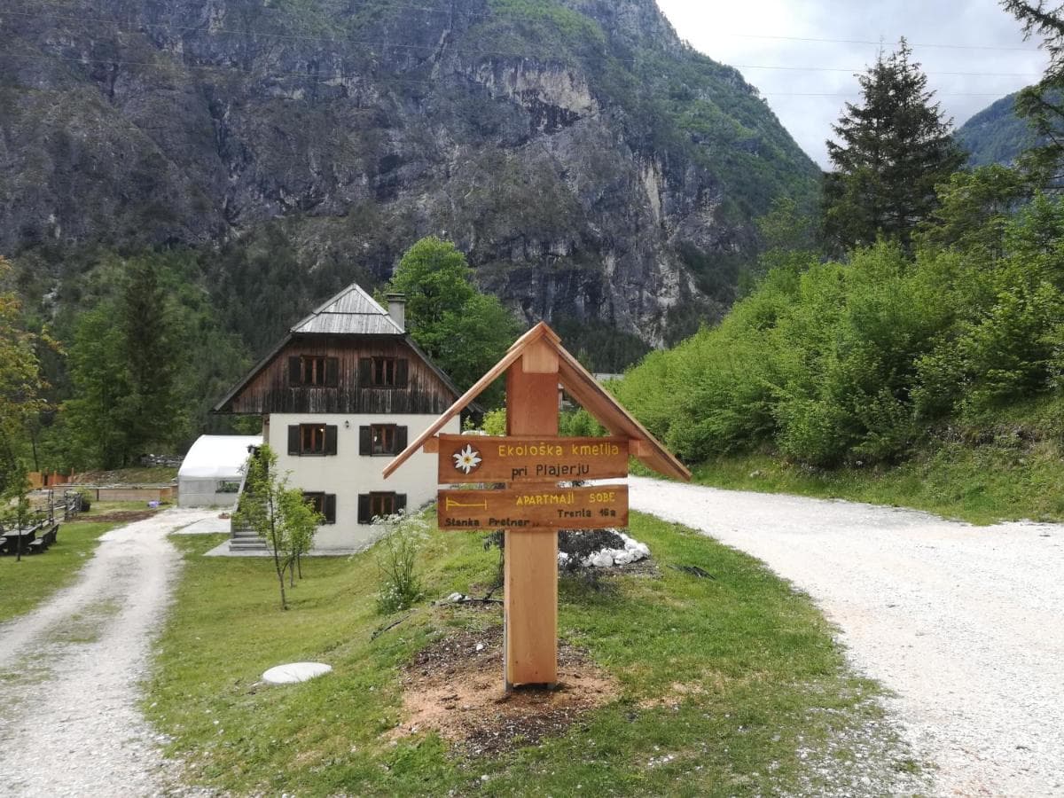 Wooden signpost near a house with a gravel road leading into steep, green mountains.