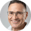 Close-up portrait of a smiling man wearing glasses against a light gray background.