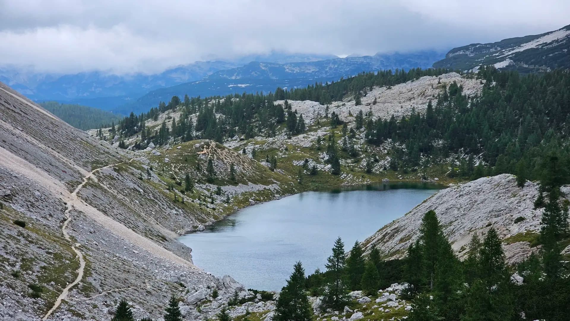 Alpine lake surrounded by rocky slopes, pine trees, and hiking trails in the Julian Alps.