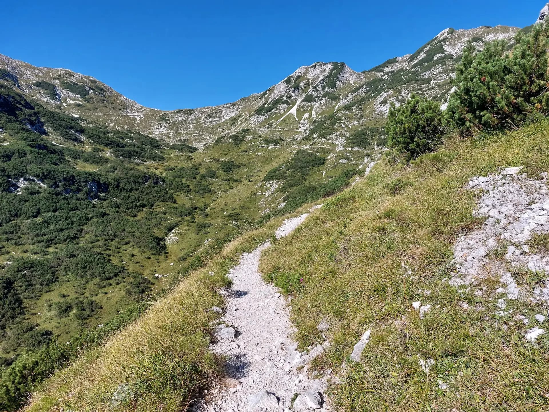 Hiking trail winding through the Julian Alps with green mountain slopes and rocky terrain.
