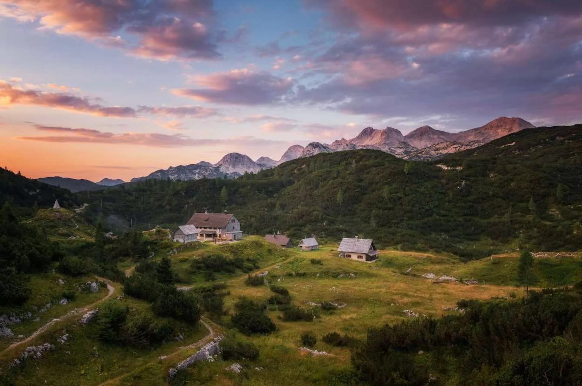 Mountain huts in a green valley with rugged peaks at sunset, Komna Plateau.