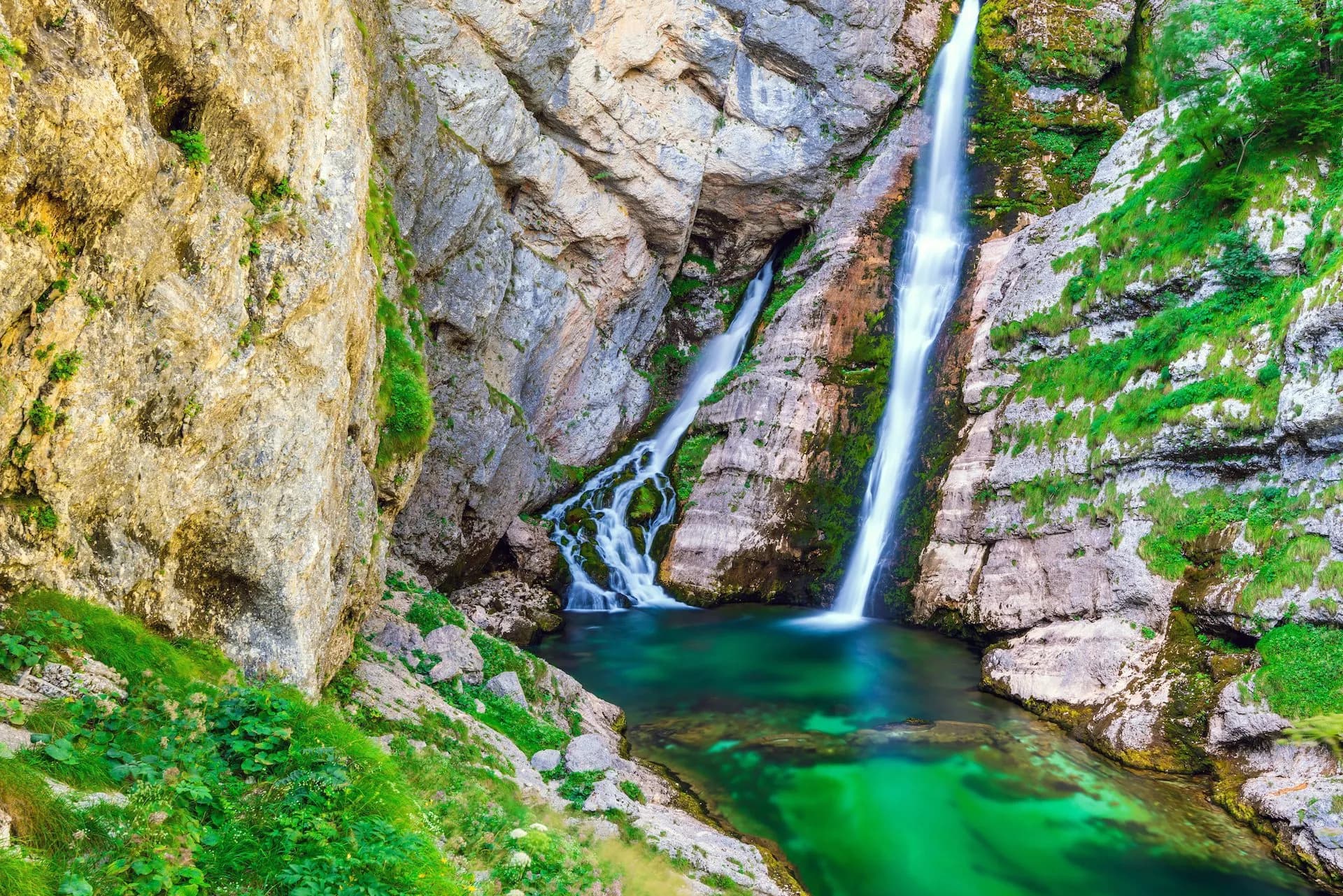 Savica Waterfall cascading down rocky cliffs into a bright emerald pool in the mountains