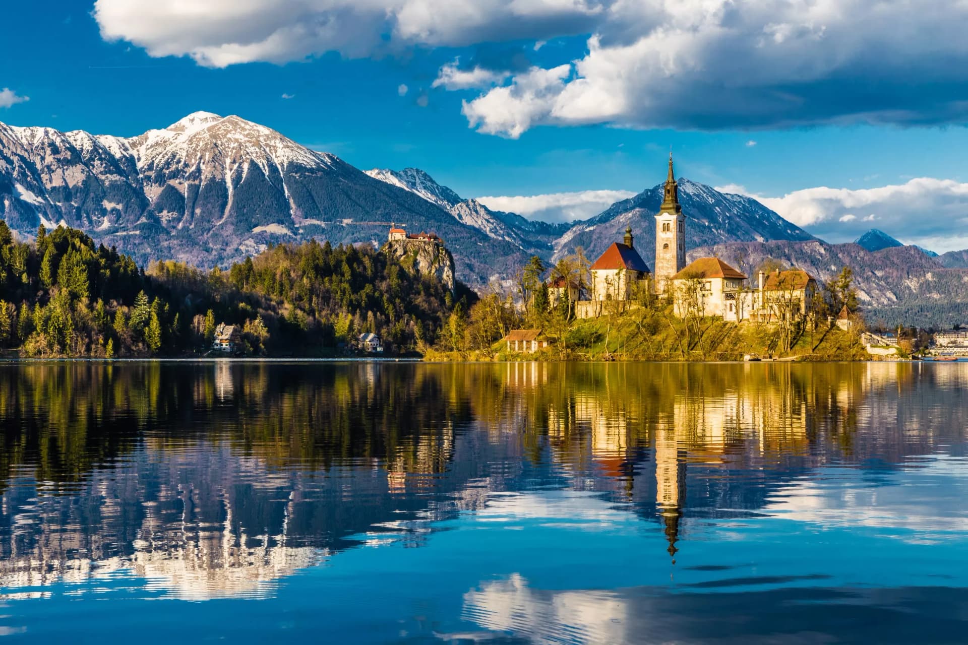 Lake Bled with church island and snow-capped mountains reflected in the water.