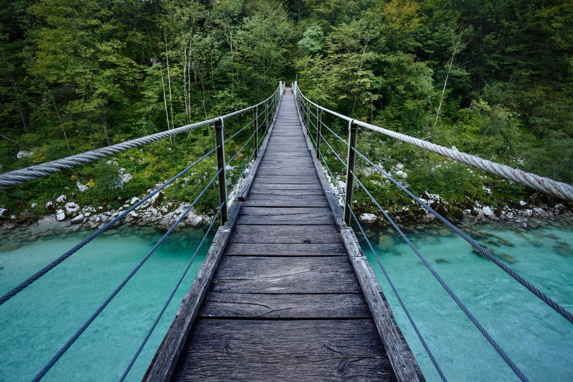 Wooden suspension bridge over turquoise Soca river in Triglav National Park forest.