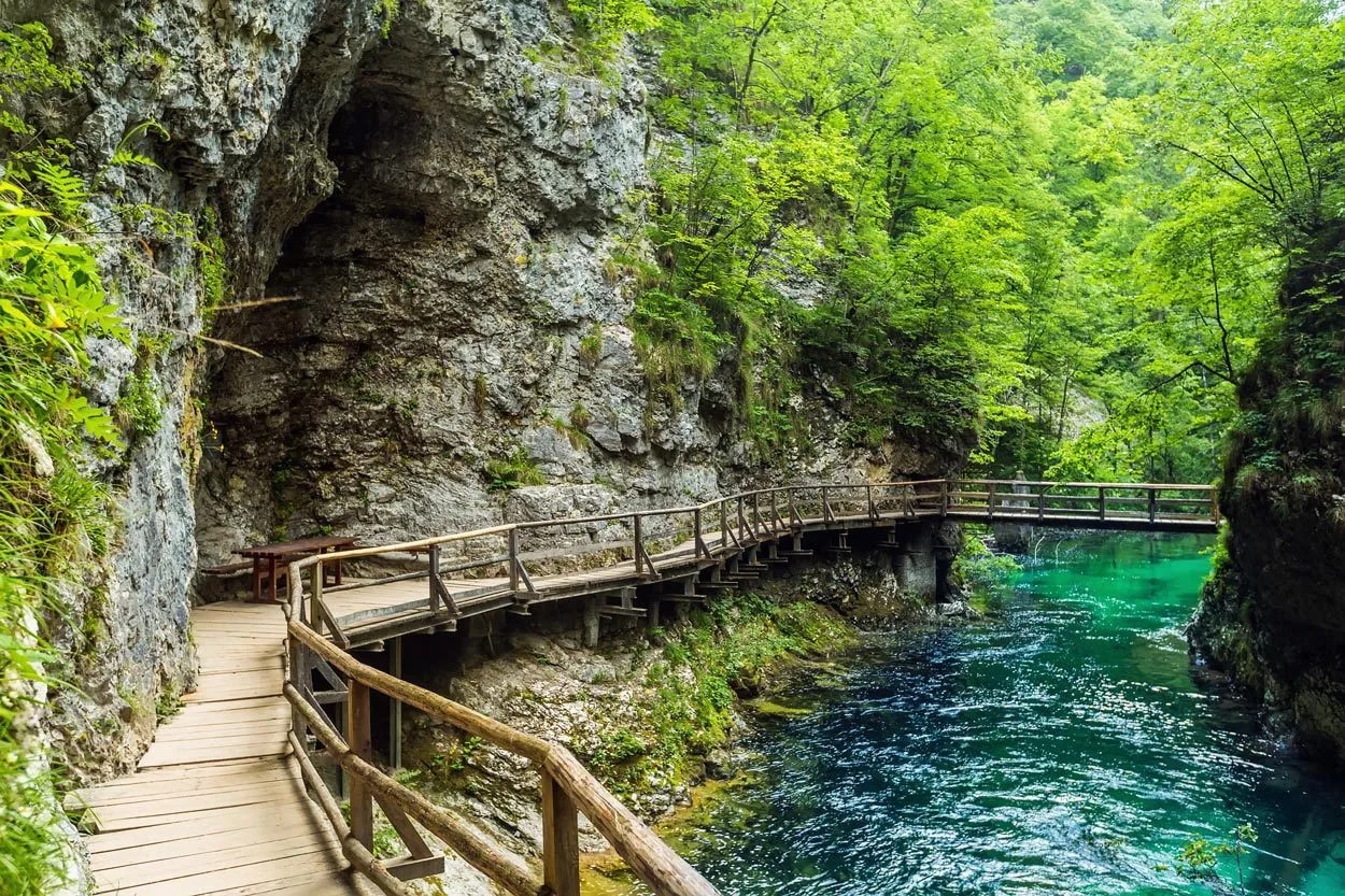 Wooden walkway along Vintgar Gorge with turquoise river and lush green forest.