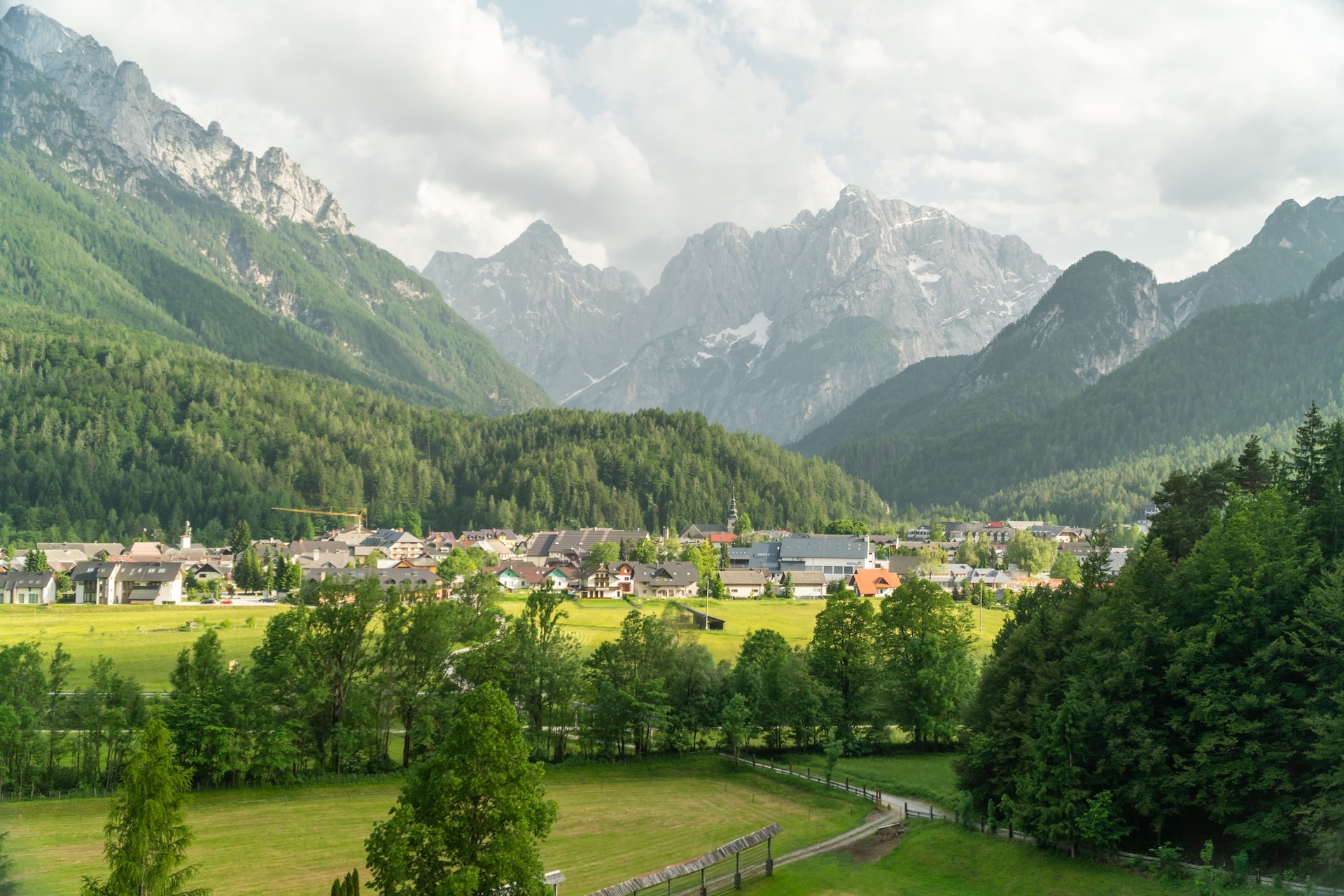 Alpine village nestled in a valley surrounded by green forests and jagged, snow-dusted mountains.