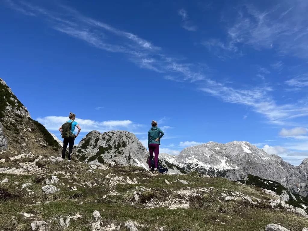Hikers overlooking rocky mountains with snow patches under a bright blue sky near Viševnik.