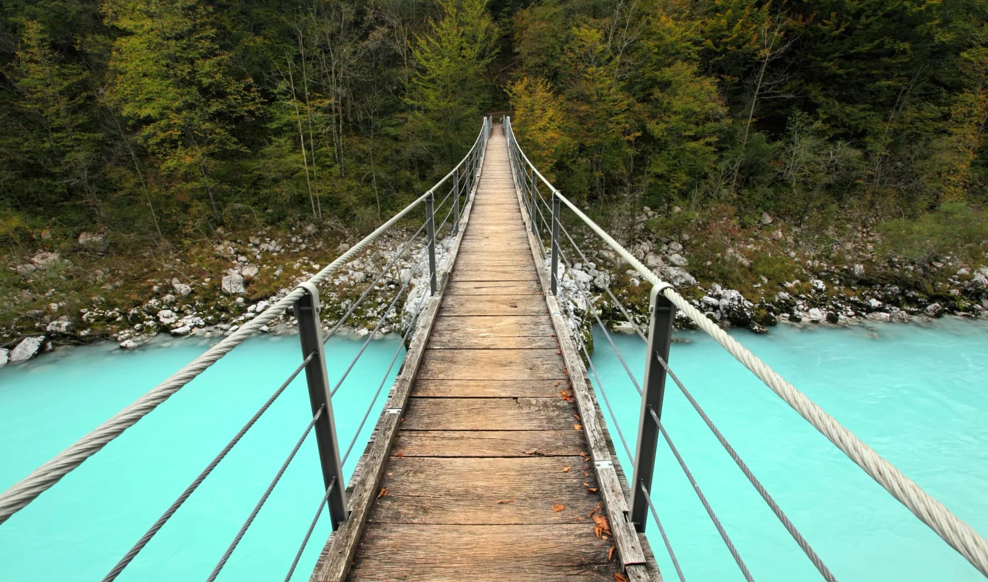 Wooden suspension bridge over bright turquoise river surrounded by dense forest