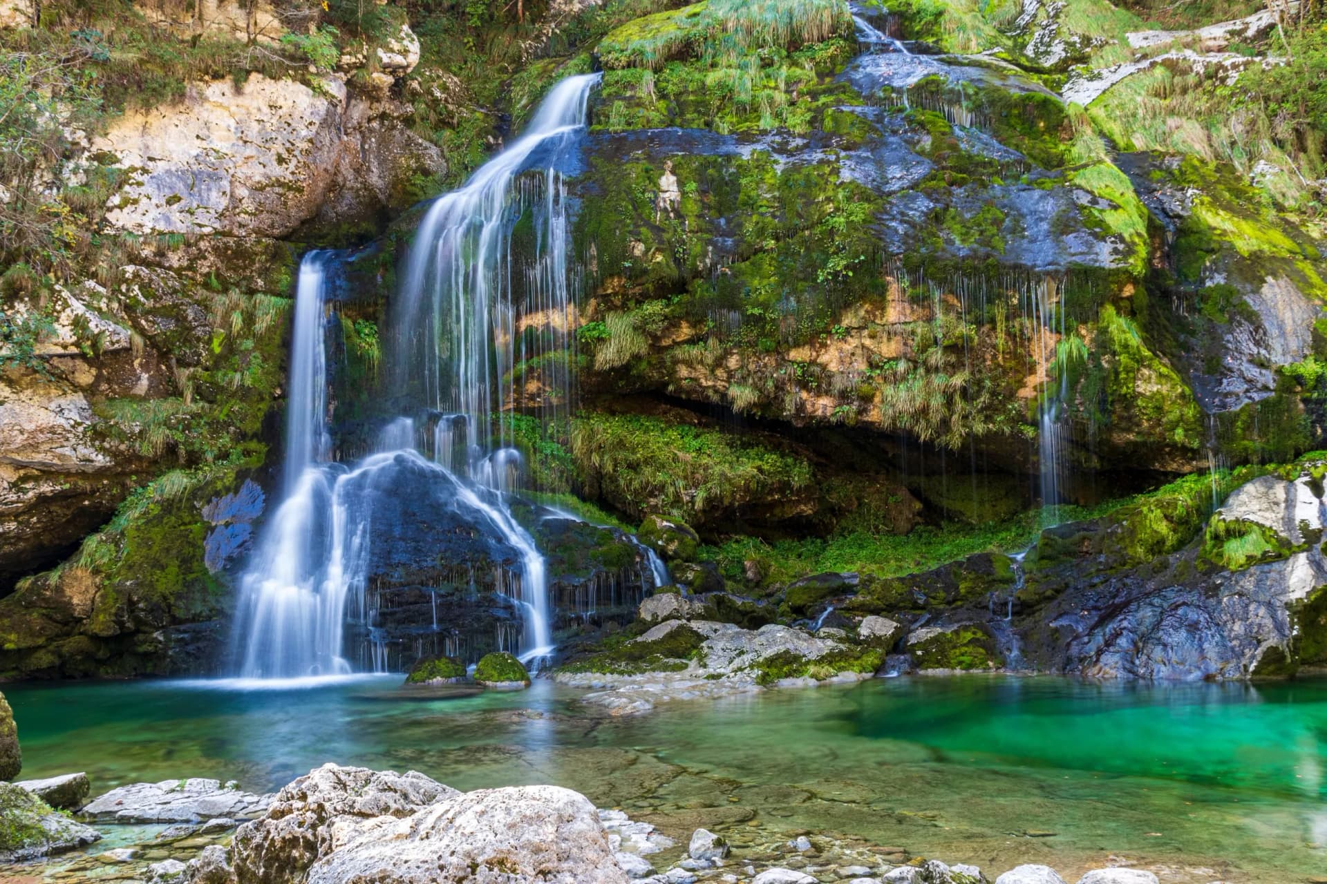 Waterfall cascading over mossy rocks into a clear, emerald green pool at Virje.