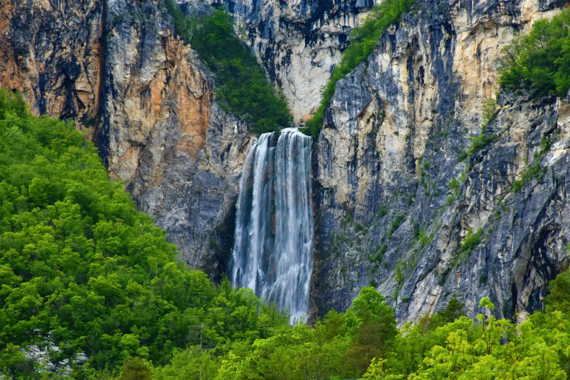 Boka Waterfall cascading down steep cliffs surrounded by vibrant green forest near Bovec.