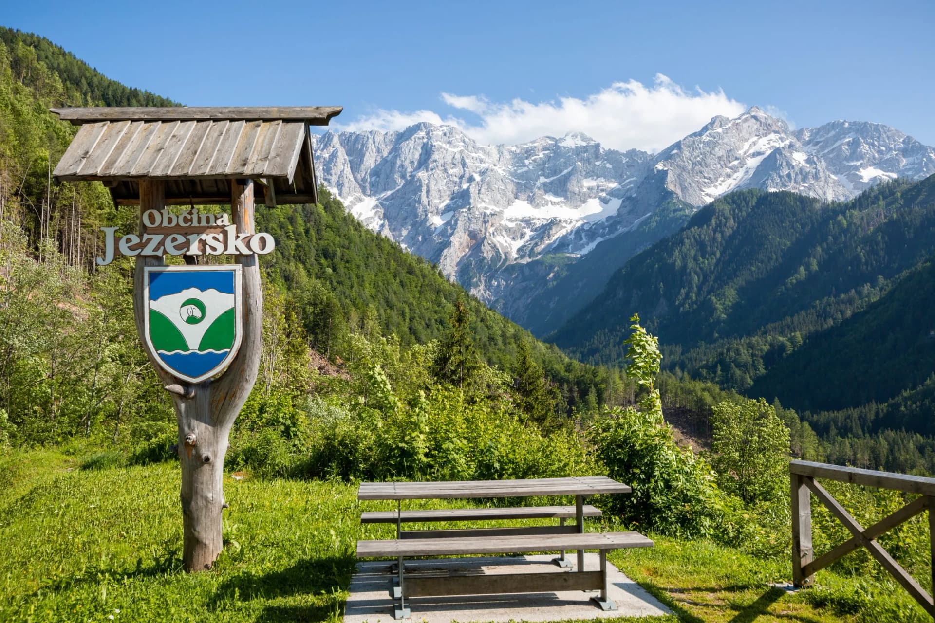 Jezersko municipality sign with picnic table overlooking Kamnik-Savinja Alps peaks with snow.