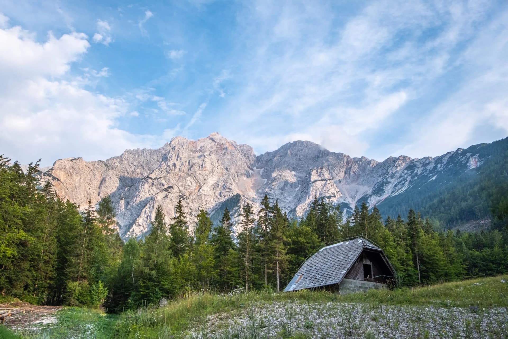 Small wooden hut in Zgornje Jezersko meadow with Kamnik-Savinja Alps backdrop.
