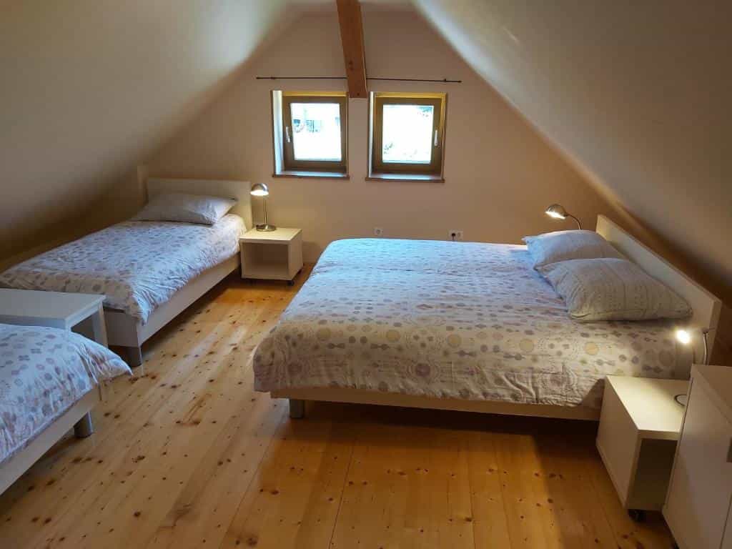Attic bedroom with three beds, light wood floors, and two small windows under the sloped ceiling.