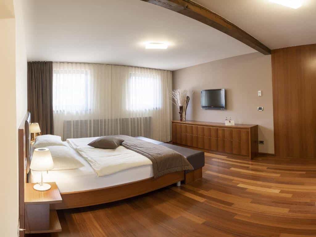 Modern hotel bedroom with wooden floors, a large bed, and a wall-mounted television.