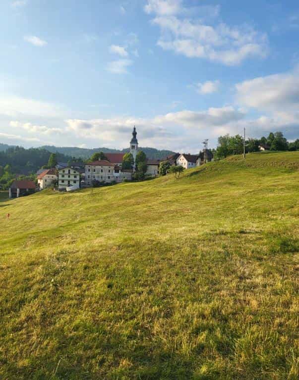 Village with church steeple nestled in green hills under a blue, cloudy sky