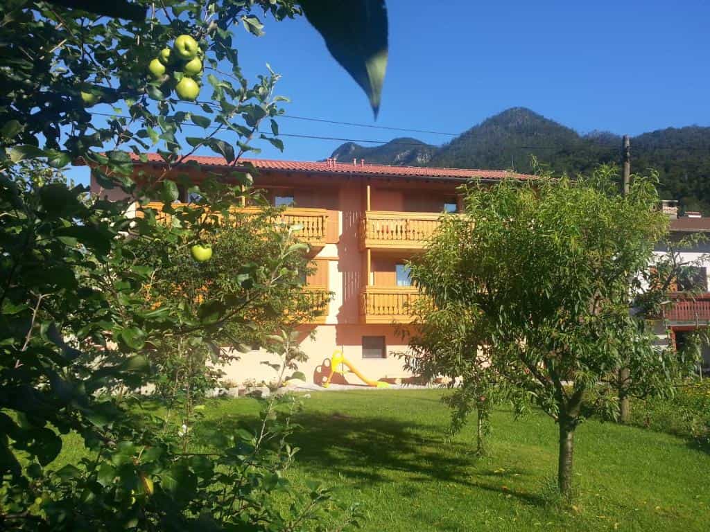 Building with wooden balconies in a green garden with fruit trees and mountains in the background.