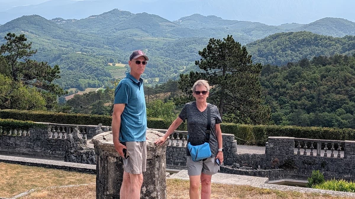 Two people standing on a terrace overlooking rolling green hills and mountain ranges