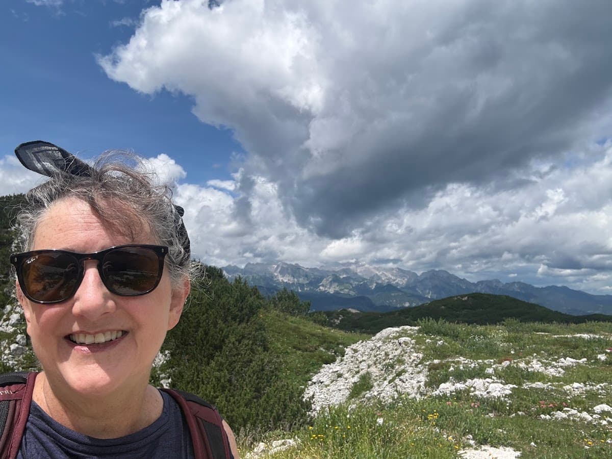 Hiking selfie with mountain peaks and cloudy sky in background
