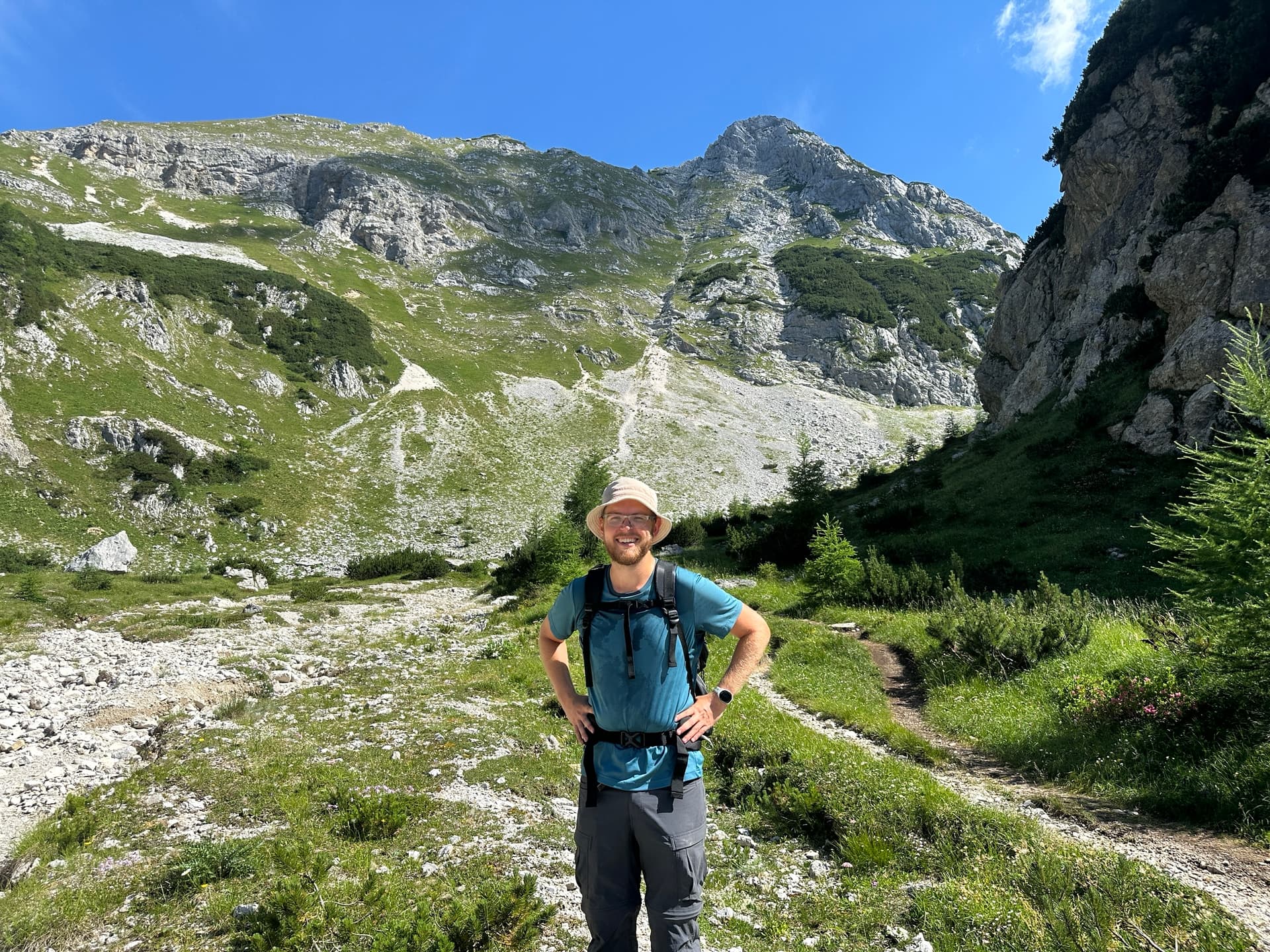 Hiker with backpack standing on alpine trail in limestone valley under blue sky