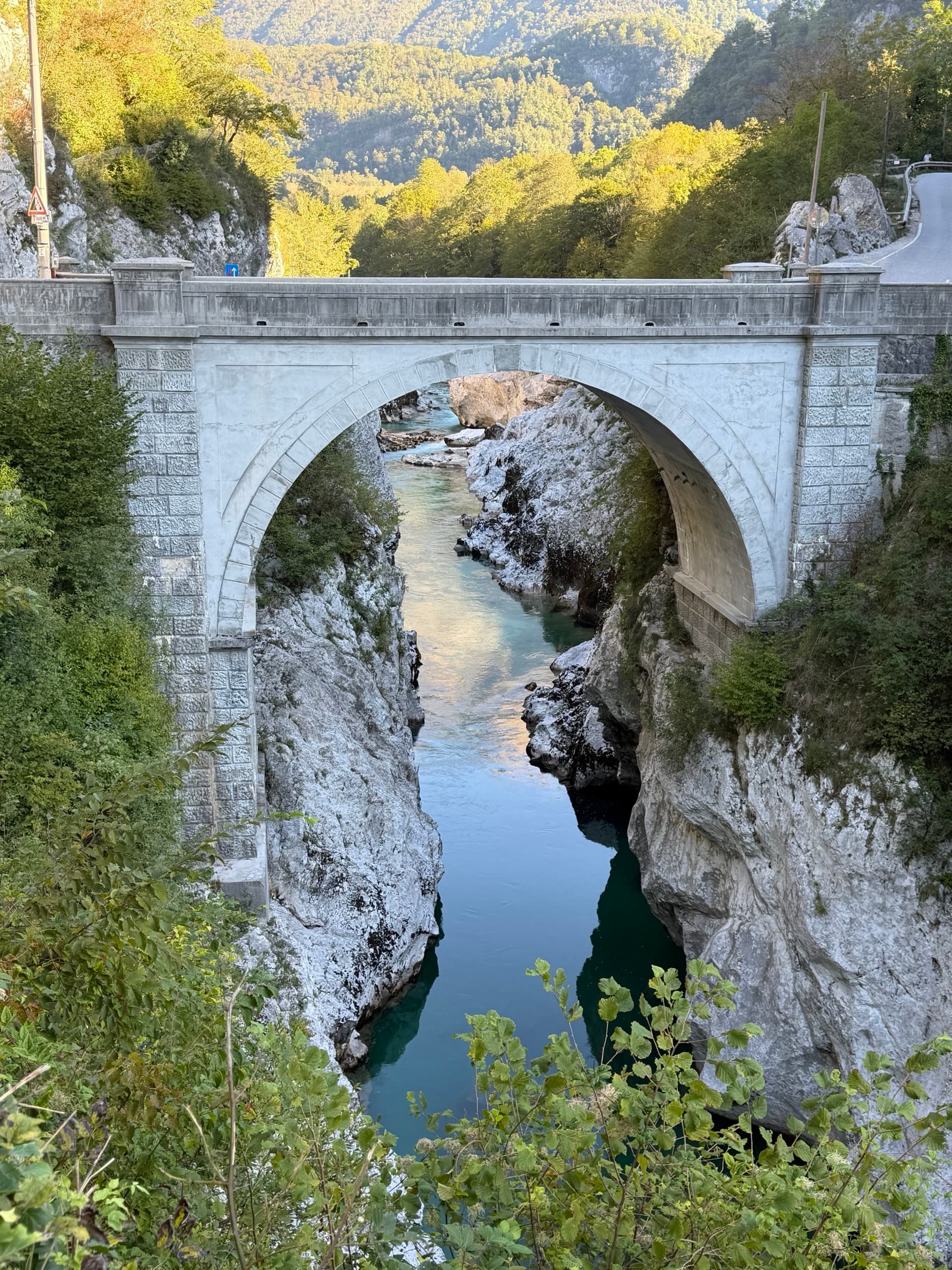Stone arch bridge over emerald river gorge with rocky cliffs and trees