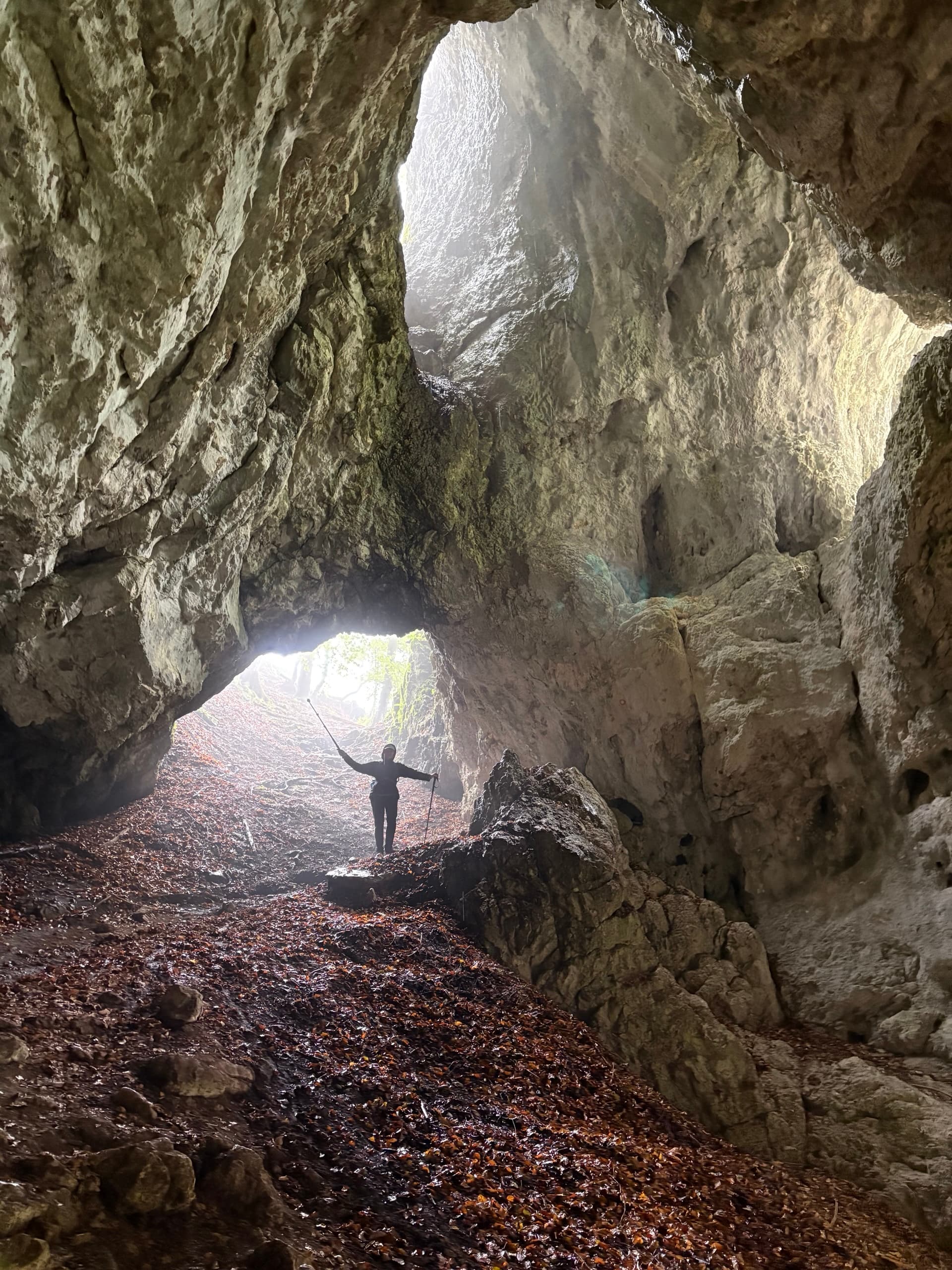Hiker standing in large limestone cave arch with light streaming through openings