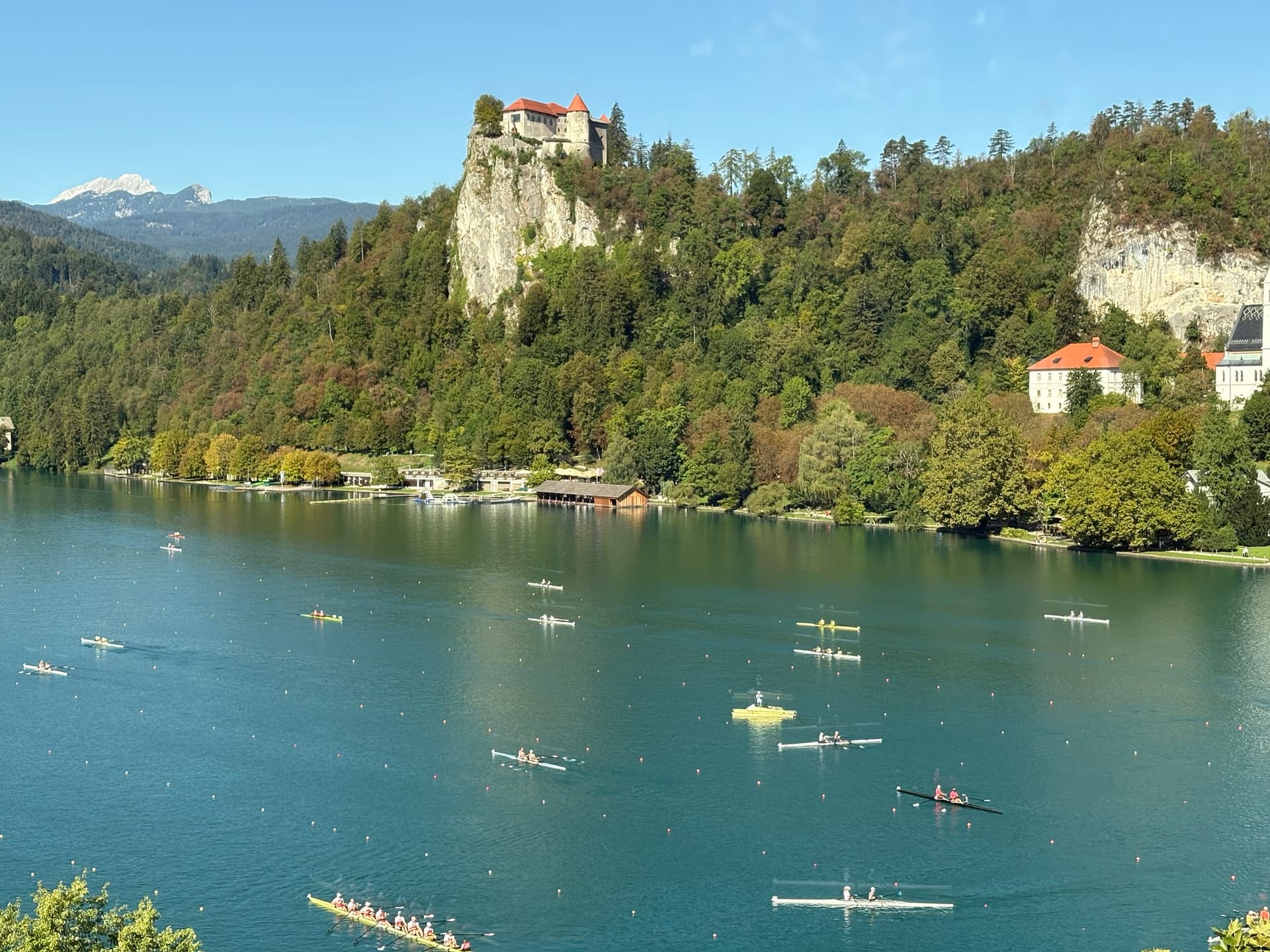 Lake Bled castle on cliff above water with rowing boats on the lake and surrounding forest