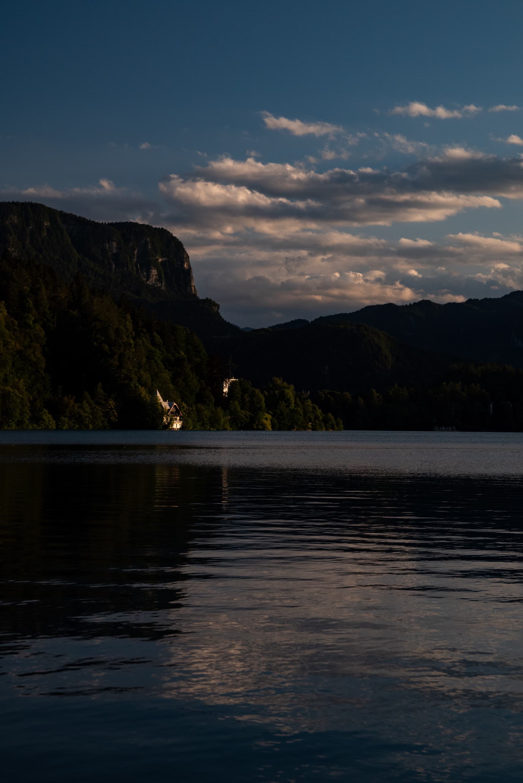 Still mountain lake at dusk with dark forested shoreline and clouds overhead