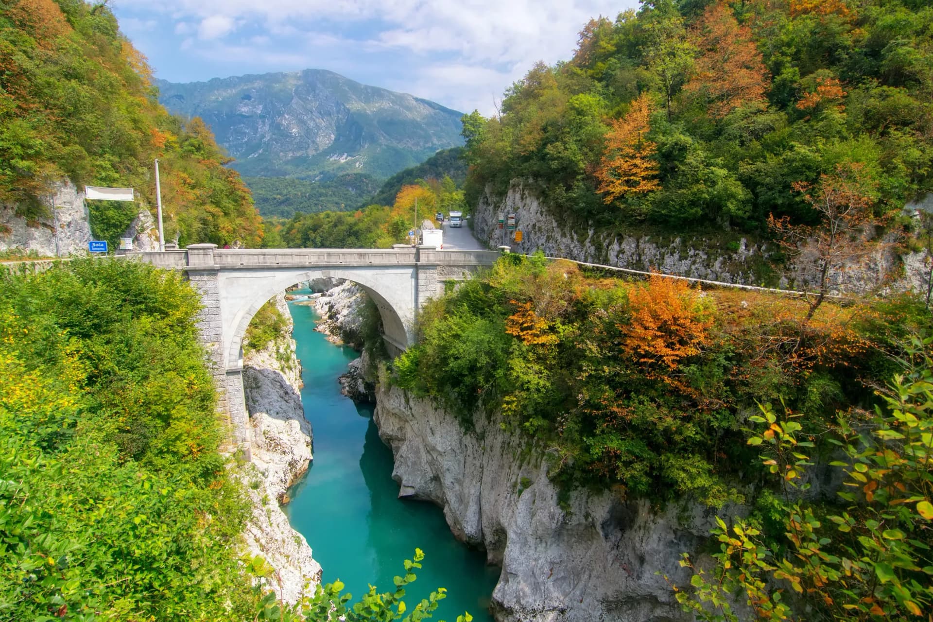 Napoleon's Bridge near Kobarid over turquoise river canyon with autumn foliage and mountains.