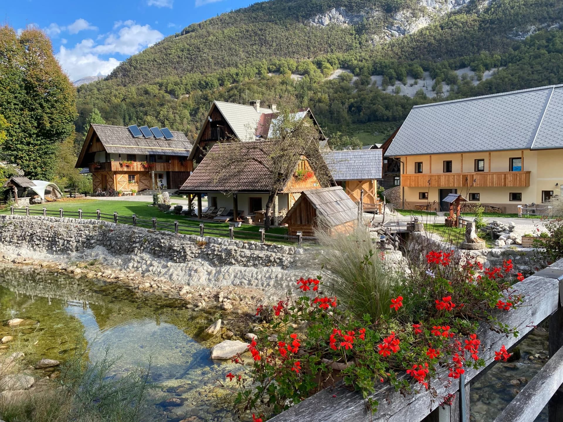 Alpine village of Stara Fužina, Slovenia, with traditional houses, clear stream, and forested mountains.