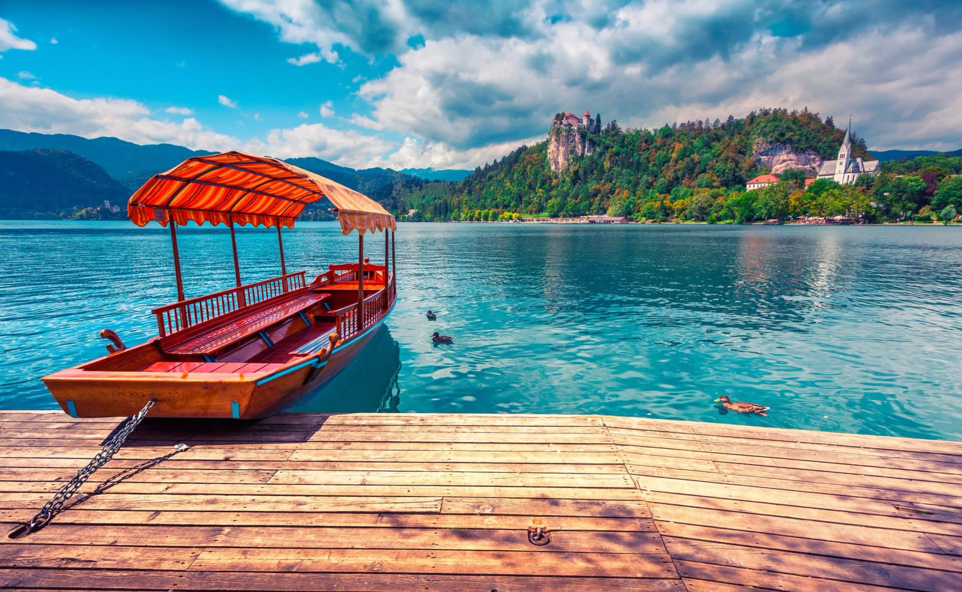 Pletna boat docked on wooden pier at Lake Bled with castle and church on forested hill.